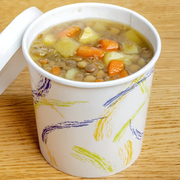 Hearty lentil soup with carrots and potatoes in a branded Soup Maison to-go cup.