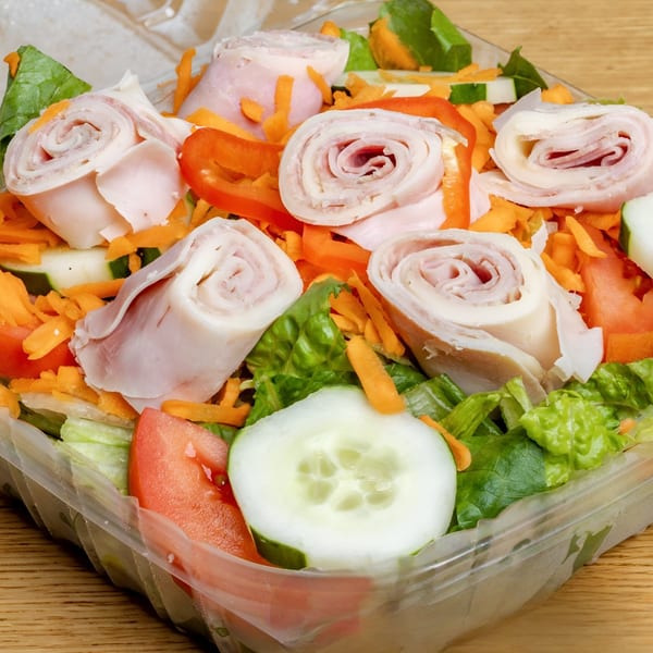 A fresh salad with ham rolls, lettuce, carrots, cucumbers, and tomatoes in a clear plastic container.