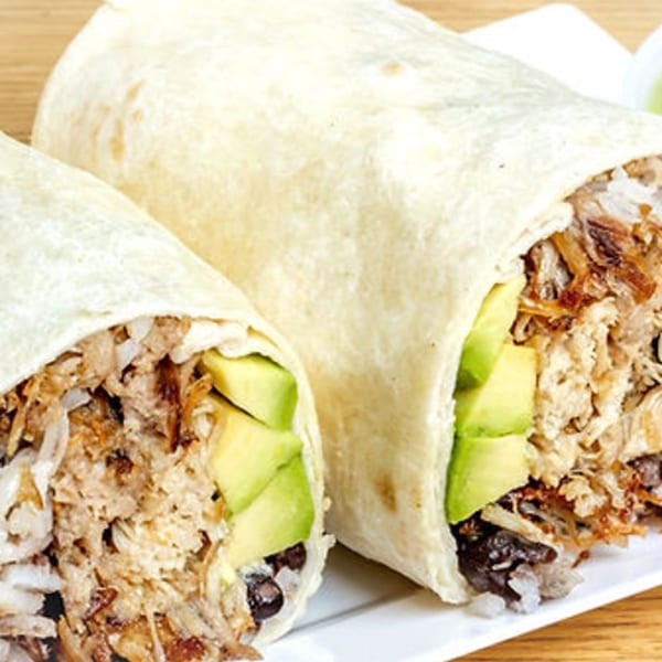 Two Latin Kitchen burritos, one cut open to show shredded meat, rice, black beans, and avocado.