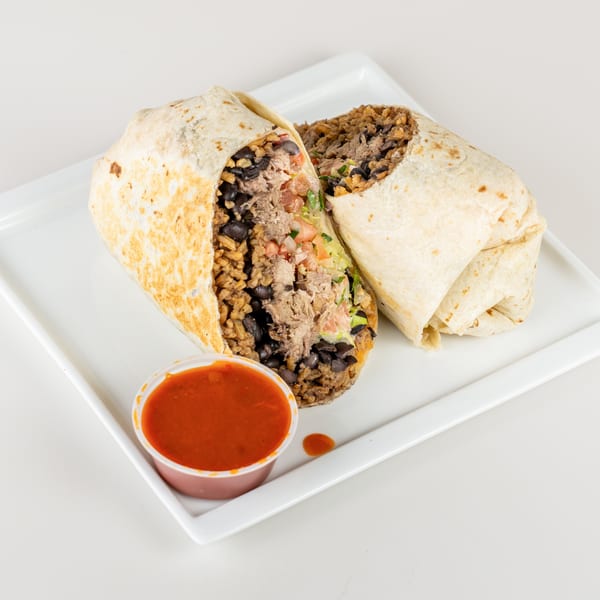 Two large burritos, one cut in half to show rice, beans, meat, and salsa, with a side of red sauce.
