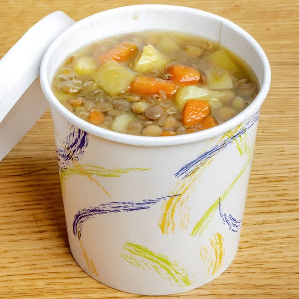 Hearty lentil soup with carrots and potatoes in a branded Soup Maison to-go cup.