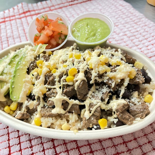 A Latin Kitchen steak bowl with rice, corn, avocado, cheese, and two side sauces.