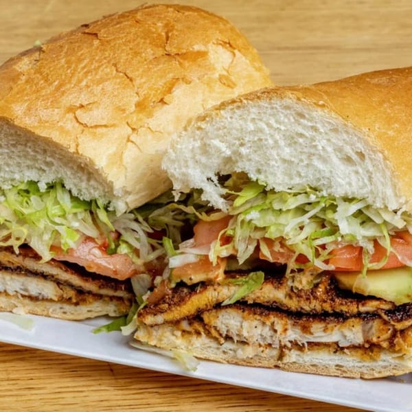 A large Latin Kitchen sandwich, cut in half, revealing layers of meat, lettuce, tomato, and avocado.